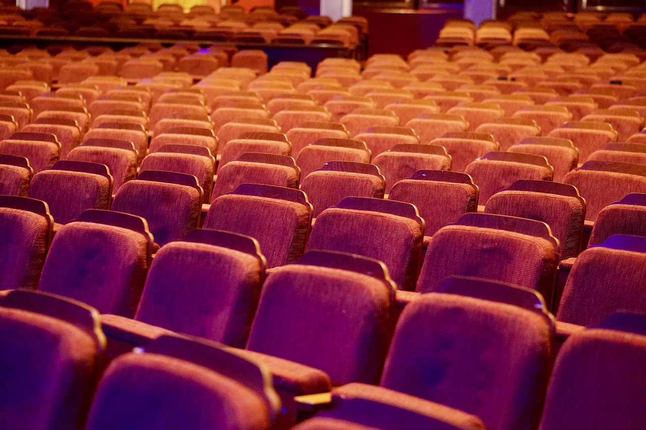 rows of movie theater seats with a pink/orange/purple filter over the image (by northpaw on Pixabay)